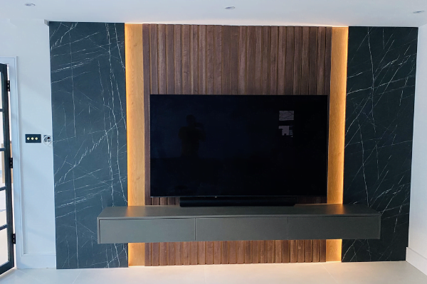 Black marble-effect and backlit walnut media wall in a Chesham entrance hall with floating TV unit