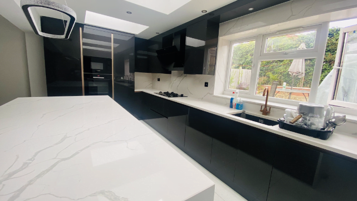 Third view of handleless black gloss kitchen in Enfield showing Calacatta quartz island, ceiling extractor, skylight and garden window
