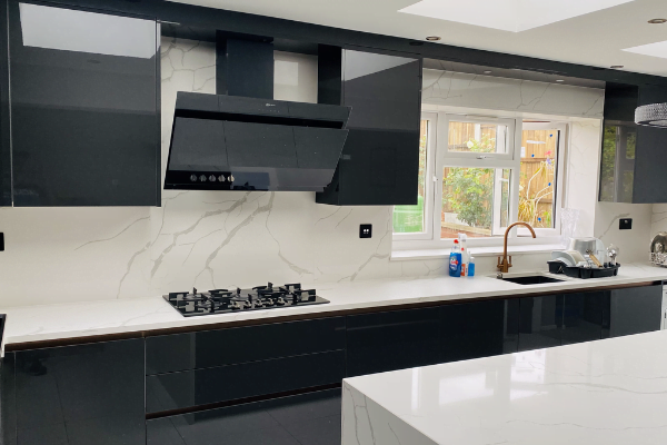 Handleless black gloss kitchen in Enfield with Calacatta marble-effect splashback, gas hob, angled extractor and rose gold tap