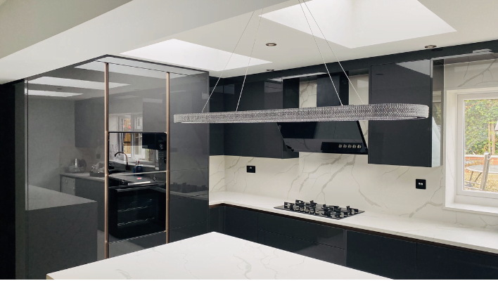 Fourth view of handleless black gloss kitchen in Enfield with crystal oval chandelier pendant, Calacatta splashback and gas hob