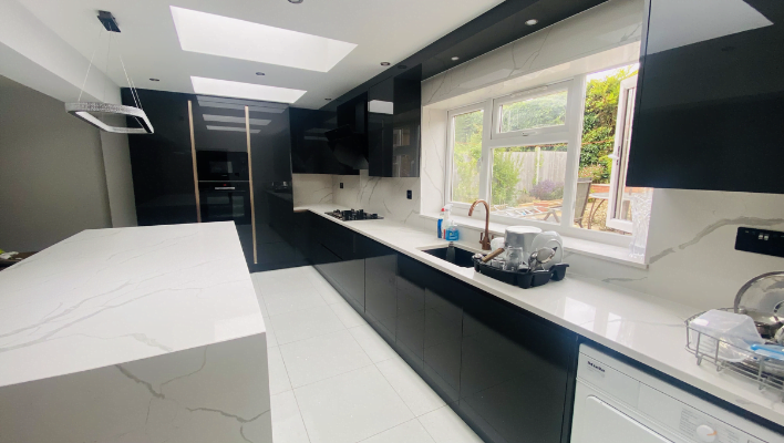 Wide view of handleless black gloss kitchen in Enfield showing full cabinet run, quartz island, skylights and garden window