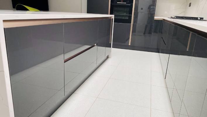 Close view of handleless black gloss kitchen island with white quartz worktop, gold trim detail and light grey porcelain floor tiles