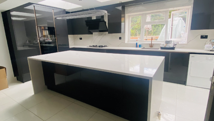Fifth view of handleless black gloss kitchen in Enfield showing white Calacatta quartz island from opposite end with full cabinet run