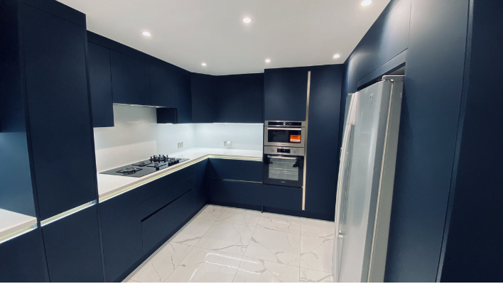 Daylight view of handleless navy blue matt kitchen in Edgware with integrated double oven, gas hob, American fridge and white quartz worktop