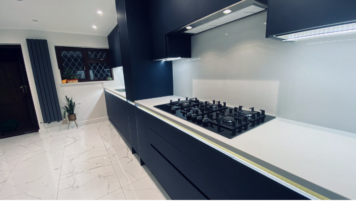 Handleless navy matt kitchen in Edgware with white quartz worktop, integrated gas hob, gold finger-pull trim and ceiling extractor
