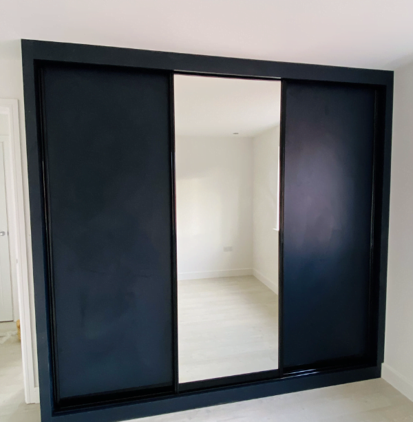 Matt black sliding wardrobe with full-height mirrored centre door and white fitted interior