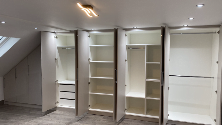 White matt wardrobe carcassed to a sloped loft ceiling with hinged doors following the roofline