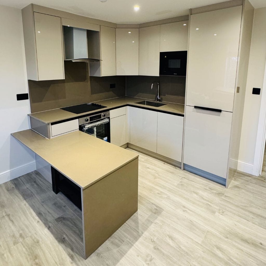 Handleless cream high-gloss kitchen with mocha quartz worktop and splashback, compact island and integrated oven and microwave