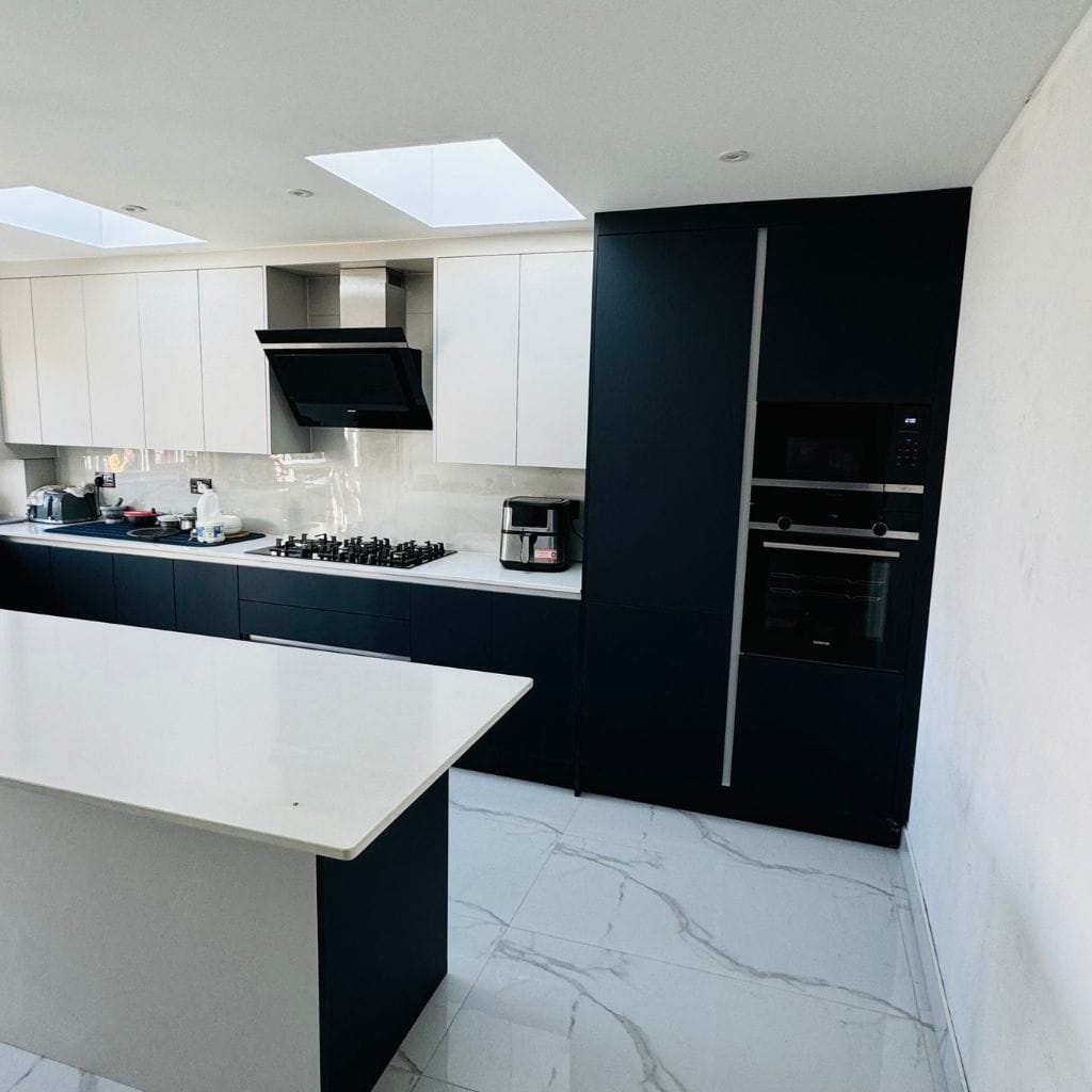 Handleless navy and white kitchen showing full-height appliance tower with integrated oven and microwave, twin skylights and quartz island