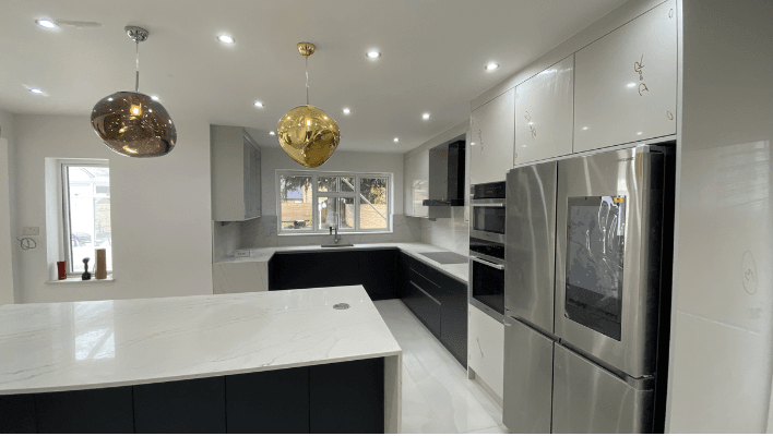 Handleless navy and white kitchen with American fridge freezer, gold and chrome globe pendants and white quartz island, angle two