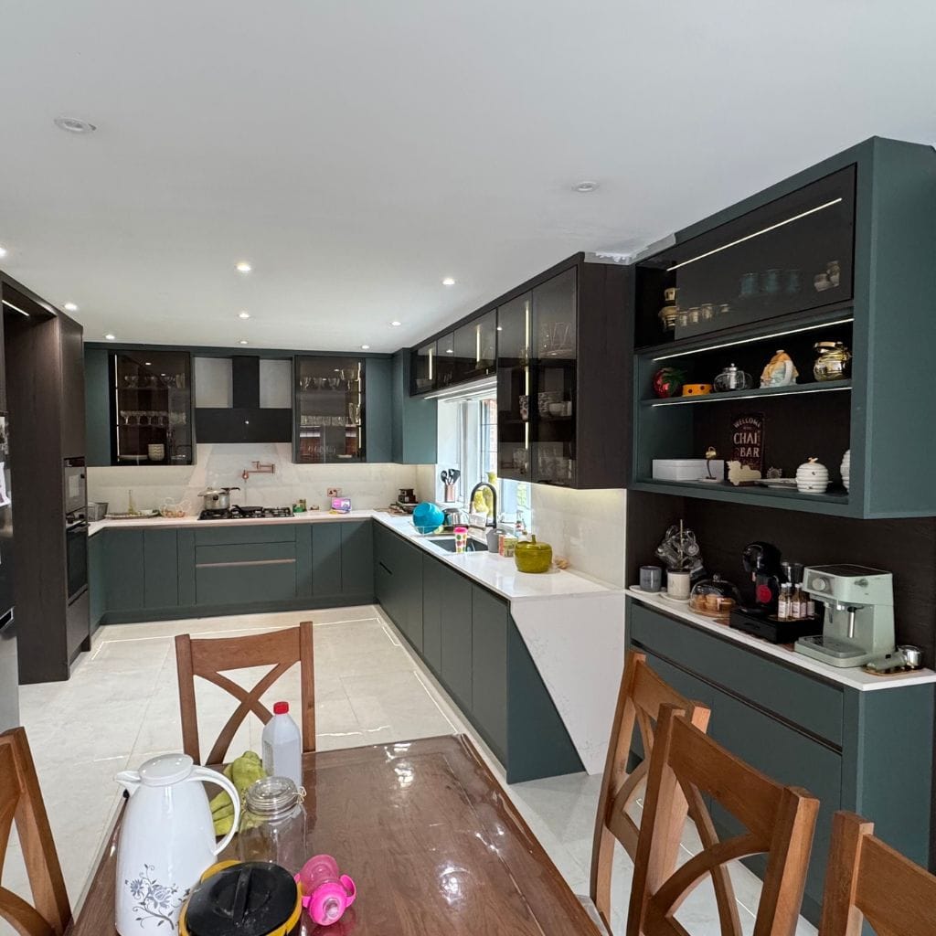 Dark teal shaker kitchen with open shelving, glass-fronted wall cabinets, white quartz worktops and integrated coffee station