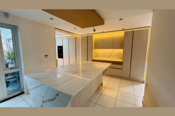 Handleless cream kitchen with large Calacatta quartz waterfall island, amber LED ceiling recess lighting and integrated appliances