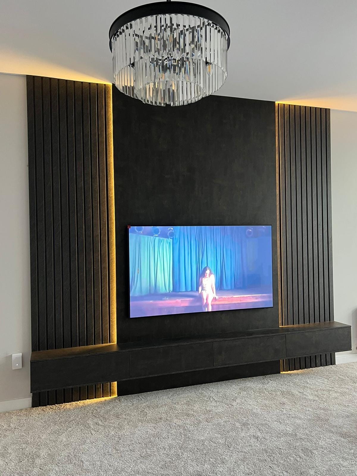Dark wood-slat media wall with warm LED backlighting, wall-mounted TV and floating storage unit